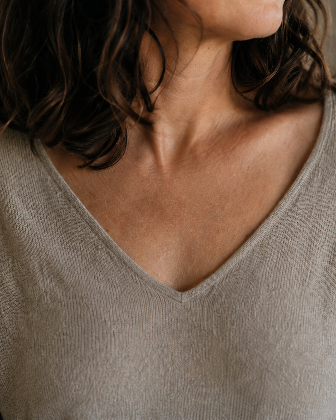 A close, warm photograph — a woman's hand resting at her collarbone and the base of her turned neck, where a sensing pendant would sit